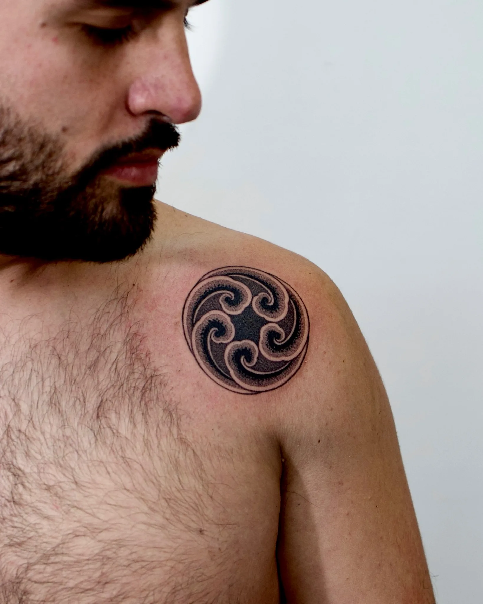 Mini blackwork Korean flash tattoo of a circular wave design with four swirling crests on the chest/shoulder. By Vezofit at Seoul Ink Tattoo, Gangnam, Seoul, South Korea.