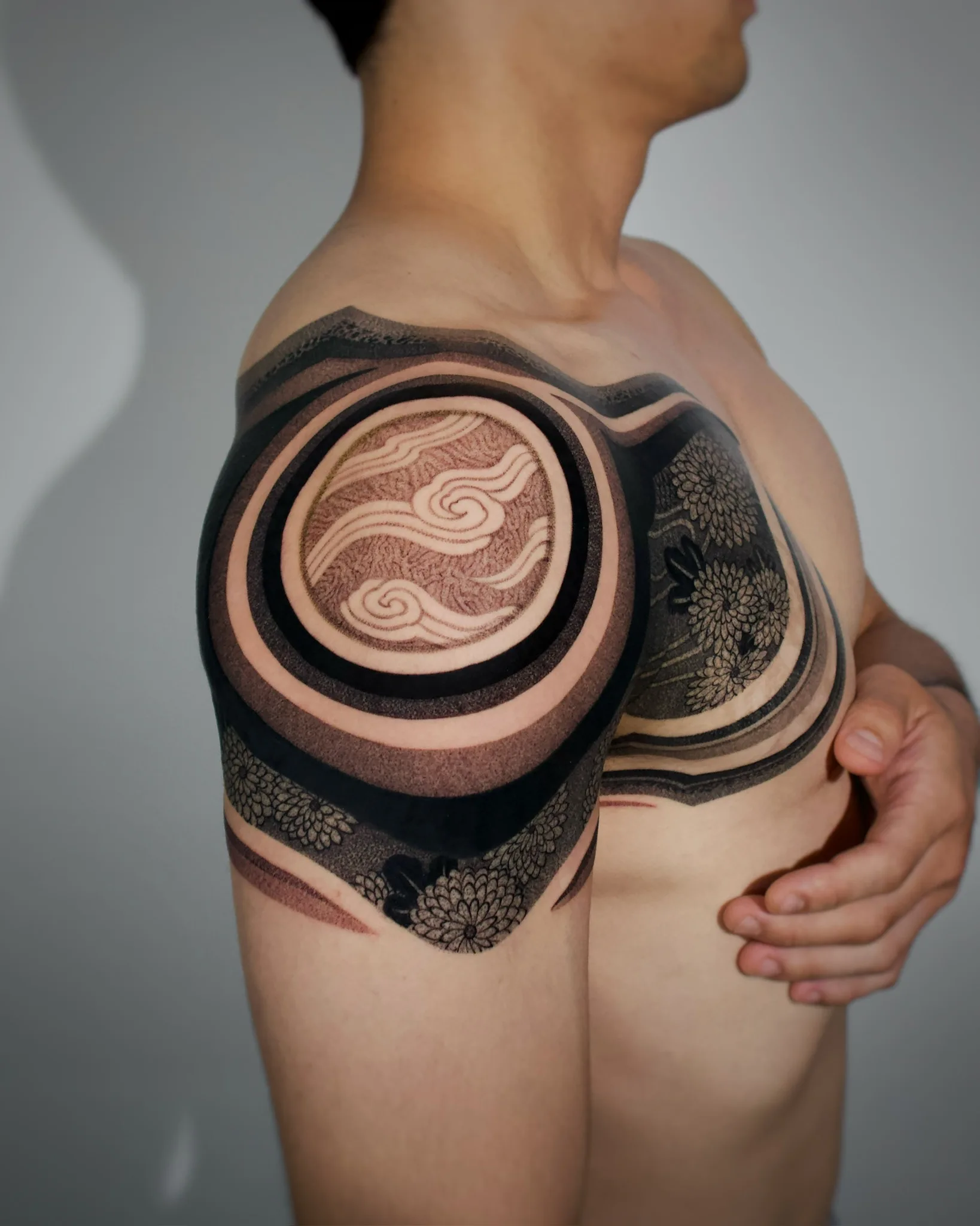 Bold blackwork Korean shoulder and chest tattoo featuring a large circular cloud motif in the center with chrysanthemum floral patterns and concentric ring shading around it. By Vezofit at Seoul Ink Tattoo, Gangnam, Seoul, South Korea.