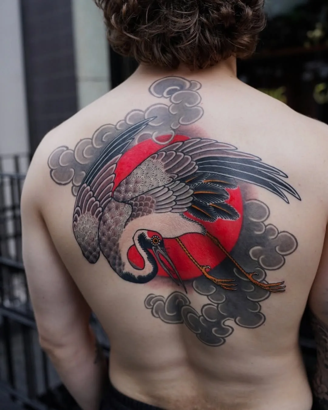 Traditional Japanese color tattoo of a crane bowing in front of a bold red sun, surrounded by grey clouds, covering the upper back. By Horimaroo at Seoul Ink Tattoo, Gangnam, Seoul, South Korea