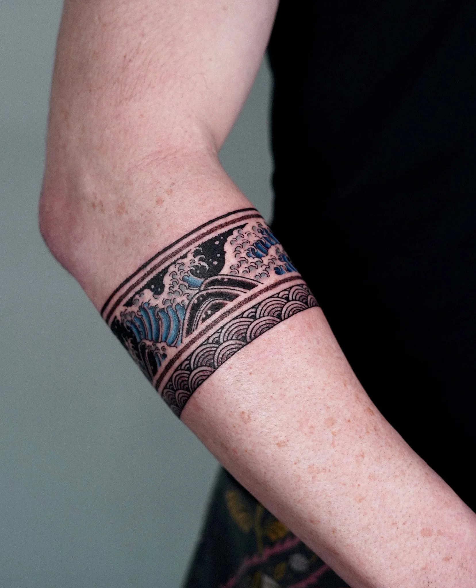 Blackwork Korean color armband tattoo on the forearm featuring crashing waves in blue and black with traditional seigaiha scale patterns on a solid black band. By Taena at Seoul Ink Tattoo, Gangnam, Seoul, South Korea