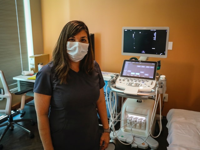 An ultrasound student standing in front of a machine, wearing scrubs, and holding a probe, ready to gain hands-on experience in the field.