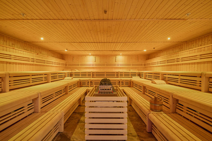 Grand sauna en bois avec bancs disposés en gradins et éclairage doux, offrant une expérience de relaxation et de détente optimale.