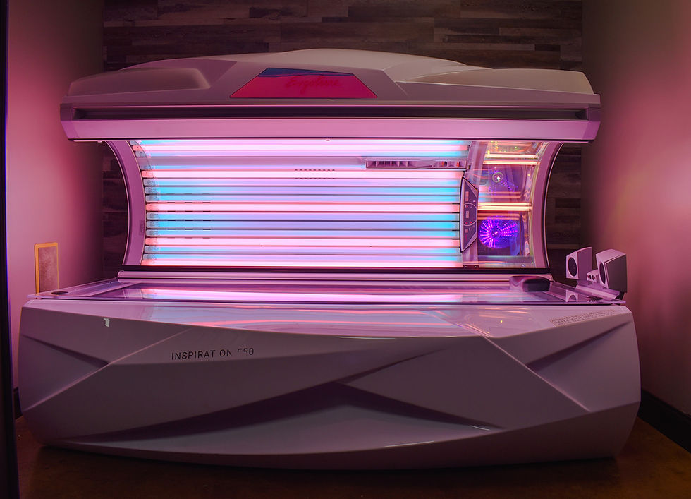 A tanning bed emits red and UV lights in a dimly lit room. The bed's sleek design features "INSPIRATION 550" text on the side.