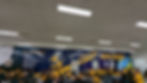 Students in yellow shirts sit at tables in a school cafeteria. A mural features a rocket, planet, and "EXPLORERS." Cafeteria rules are listed.