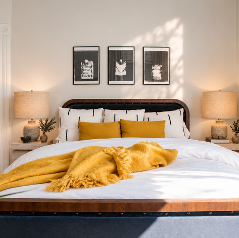 Bedroom with a black-and-walnut bed, mustard throw and pillows, framed photographs and bold art
