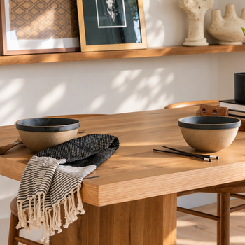 Close-up of the oak dining table with black bowls, a striped napkin and framed art above