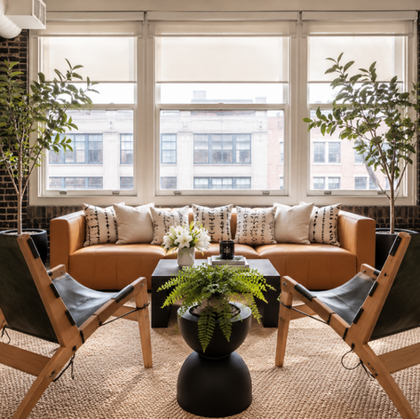Lounge by the loft windows with cognac leather sofa, mudcloth pillows, black sling chairs and fiddle-leaf trees