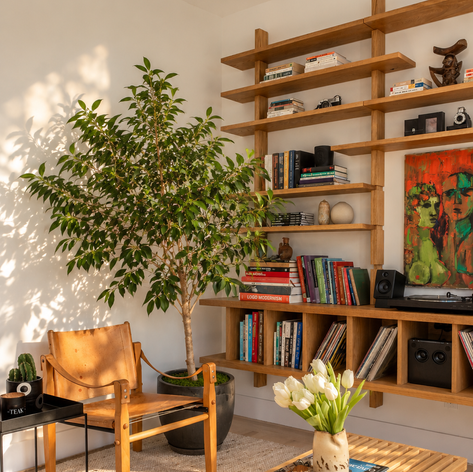 Corner of the living room with a ficus tree, oak shelving and a bench table set with tulips and books