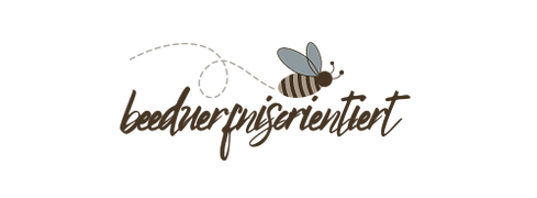 Der Schriftzug "beeduerfnisorientiert" mit einer Biene, die darüber fliegt. Der Schriftzug ist braun.