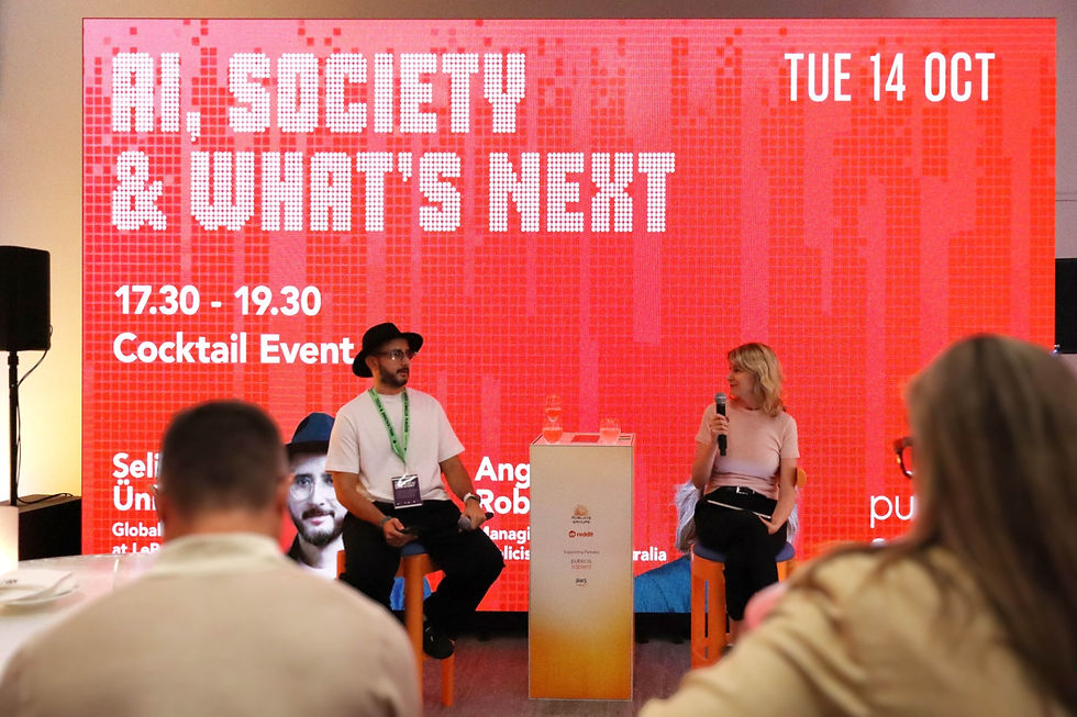 Three people stand smiling in a neutral studio setting. All wear dark clothing. Black and white image.