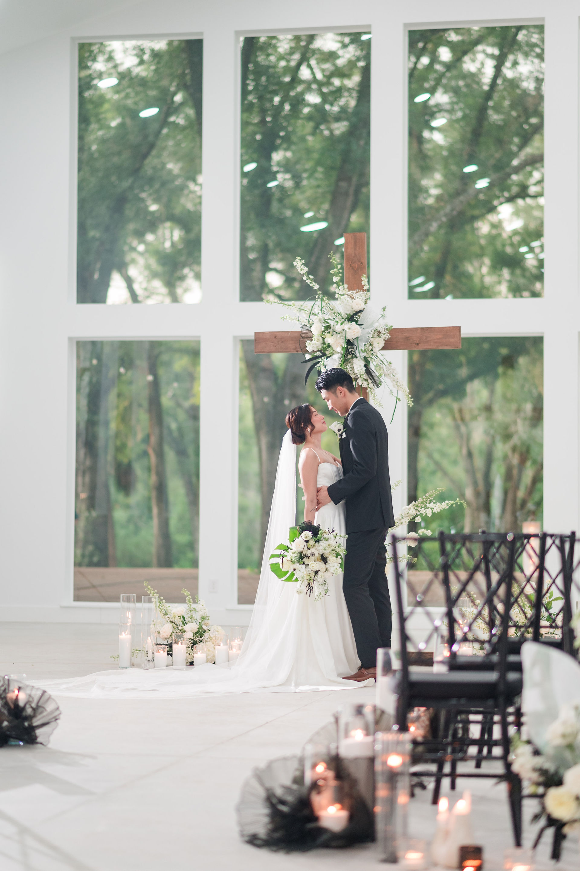 bride and groom embracing in front of the florally decorated cross at Whitewood Ranch