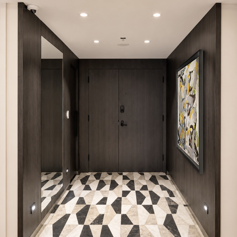 Westmount condominium entrance hall with dark wood paneling, geometric black-and-white marble flooring, a full-height mirror and abstract artwork, designed by Evolution Design.