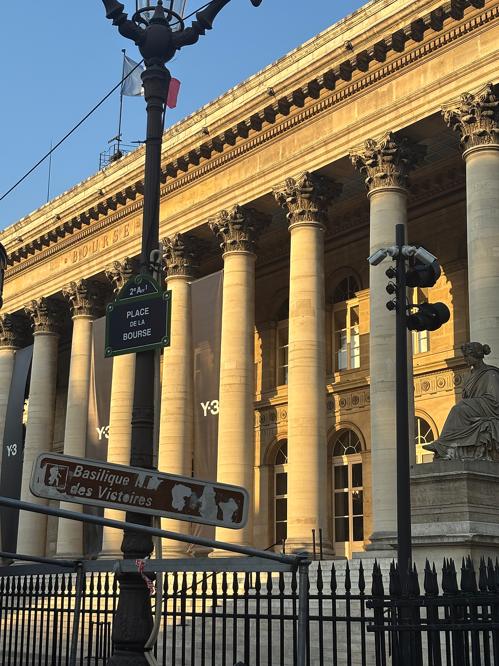 Sunlit neoclassical Bourse building in Paris with tall columns, street signs for Place de la Bourse, and clear blue sky.