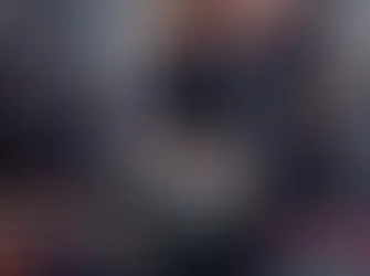 A person with a striped top and navy coat carries a quilted Chanel Flap handbag and newspaper in a cafe setting. Red and green chairs in the background.