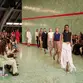 Models strut down a mint green tiled runway with a red stripe, while an audience captures the scene. The mood is fashionable and dynamic.