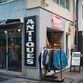 Storefront with "ANTIQUES" sign and clothes rack of colorful jackets. "STEP AHEAD" sign advertises used clothing store. Urban setting invTokyo.