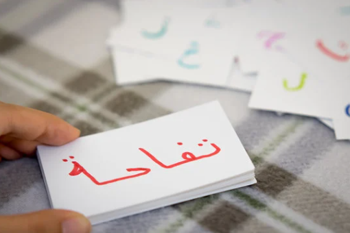 Child holding Arabic alphabet flashcards