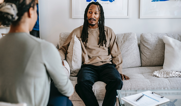 Person sitting on a couch, in conversation with another person. A clipboard and pen sits on a table to the side