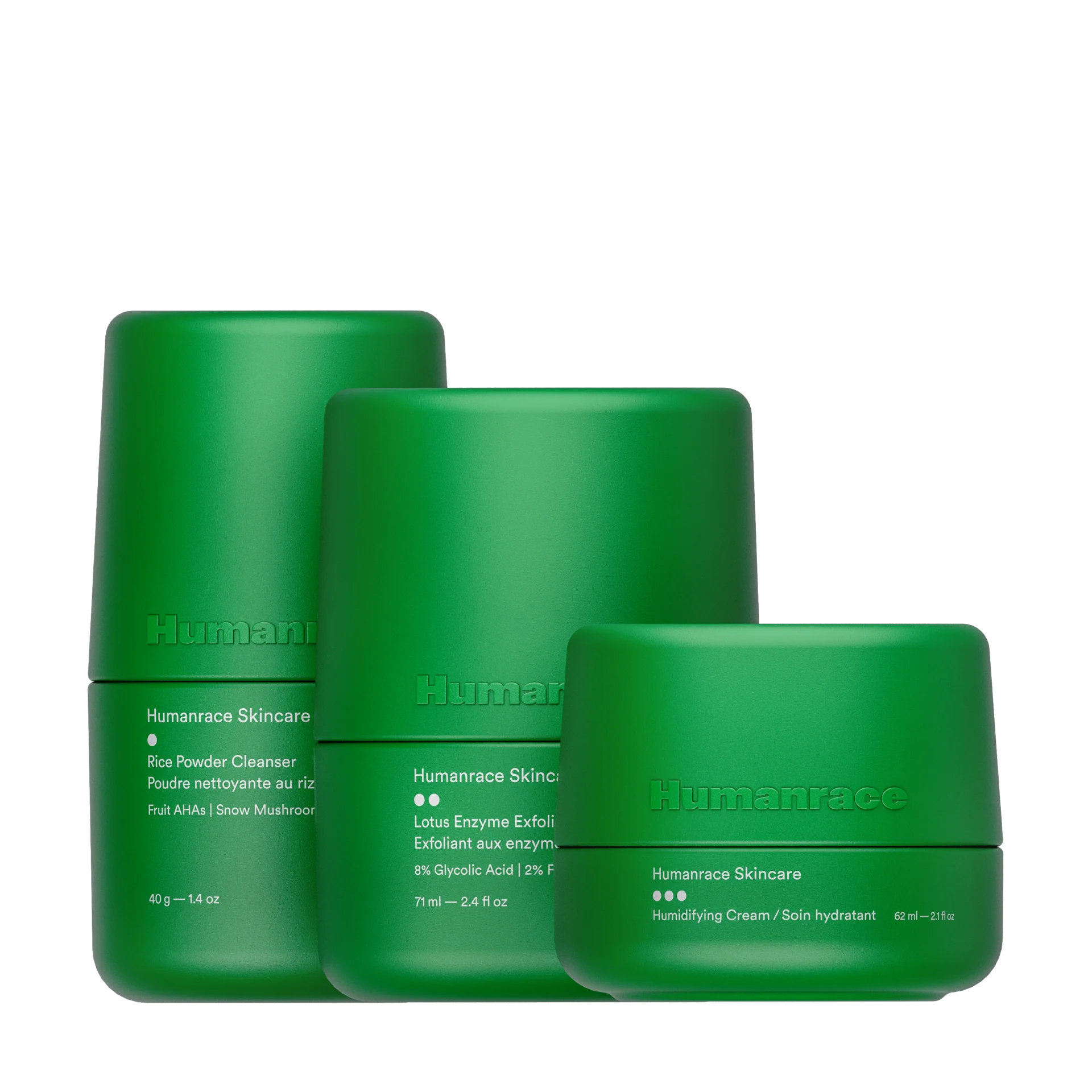 Três produtos Humanrace Skincare em embalagens cilíndricas minimalistas de cor verde-claro, dispostos em tamanhos decrescentes da esquerda para a direita contra um fundo preto. Os produtos são o Rice Powder Cleanser, o Lotus Enzyme Exfoliator e o Humidifying Cream.