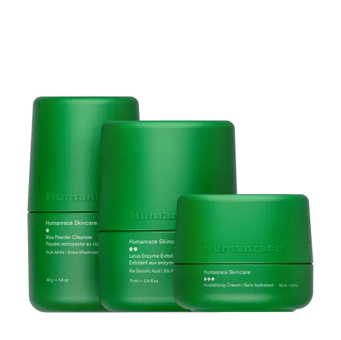 Três produtos Humanrace Skincare em embalagens cilíndricas minimalistas de cor verde-claro, dispostos em tamanhos decrescentes da esquerda para a direita contra um fundo preto. Os produtos são o Rice Powder Cleanser, o Lotus Enzyme Exfoliator e o Humidifying Cream.