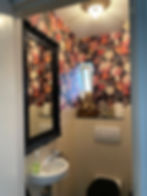 bathroom with floral wallpaper and antique black framed mirror, tiny sink, and toilet with black lid.