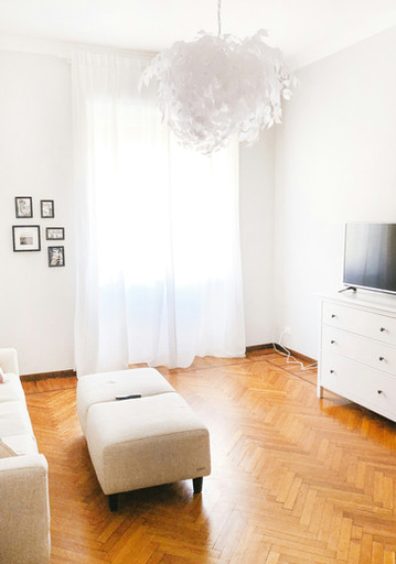 Living room with white feather chandelier, white couch, cream ottoman, and wood floors