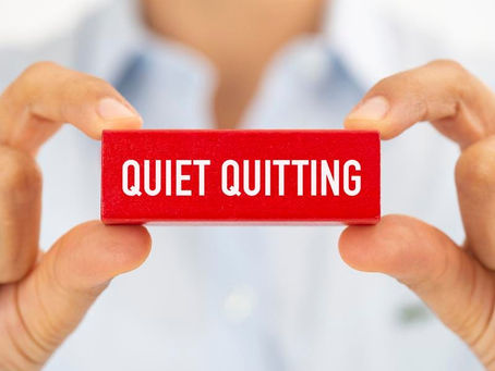Two hands hold a red block displaying the words "QUIET QUITTING," highlighting the current workplace trend of employees doing only what is specified in their job description without going beyond.