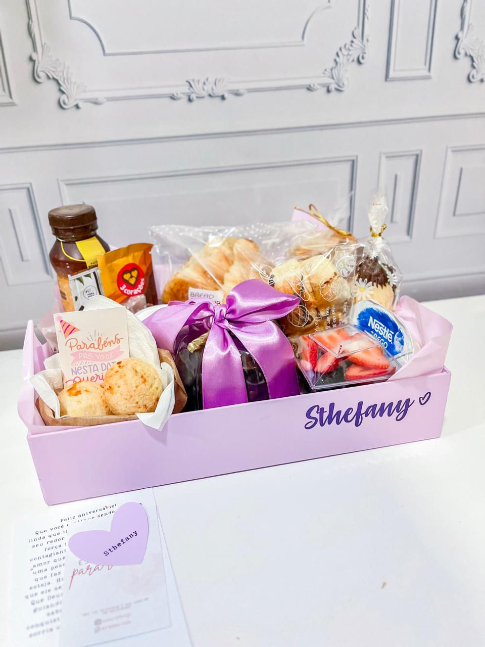 Miniatura: Cesta de café da manhã de aniversário com caixa lilás, laço rosa e doces.