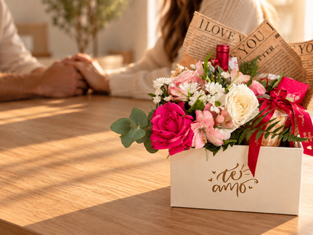 Arranjo de flores com garrafa e doce em caixa personalizada com a frase "Te amo" sobre mesa.