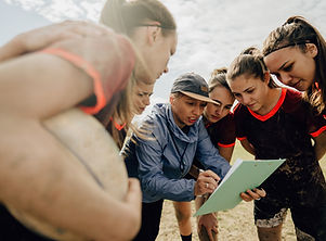 A female coach breaking down a play in a huddle where the players are focused on the play.