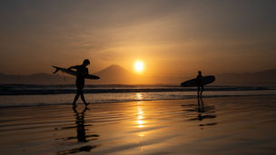 夕日の強い逆光に照らされた海辺のサーファーのシルエット
