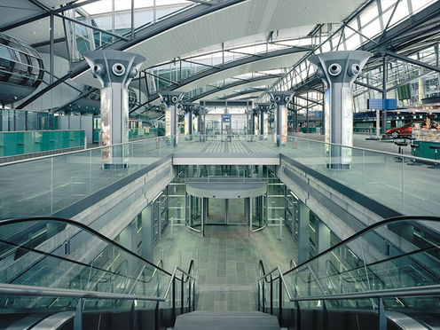 Innenansicht eines modernen Bahnhofsbereichs mit Rolltreppen und Dachkonstruktion.