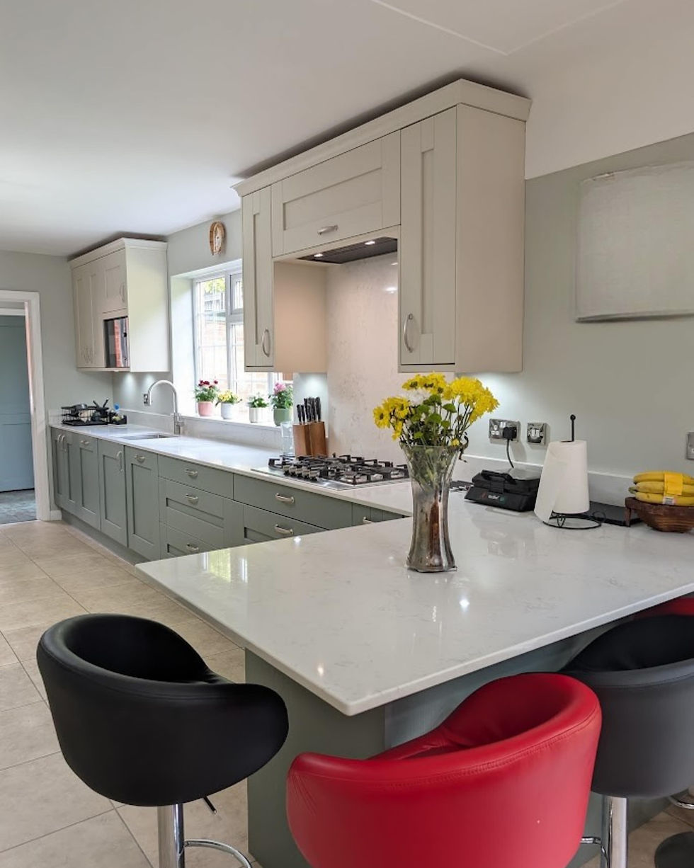 Modern kitchen with pale cabinets, white island, colorful bar stools, and a vase of yellow flowers on the counter.