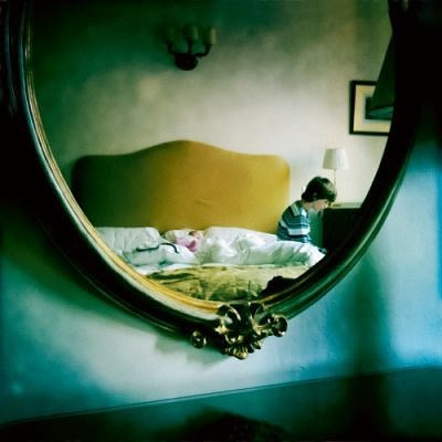 Miniature : photographie dans un miroir, on y voit un garçon sur un lit et dans ce lit un bébé habillé en rose