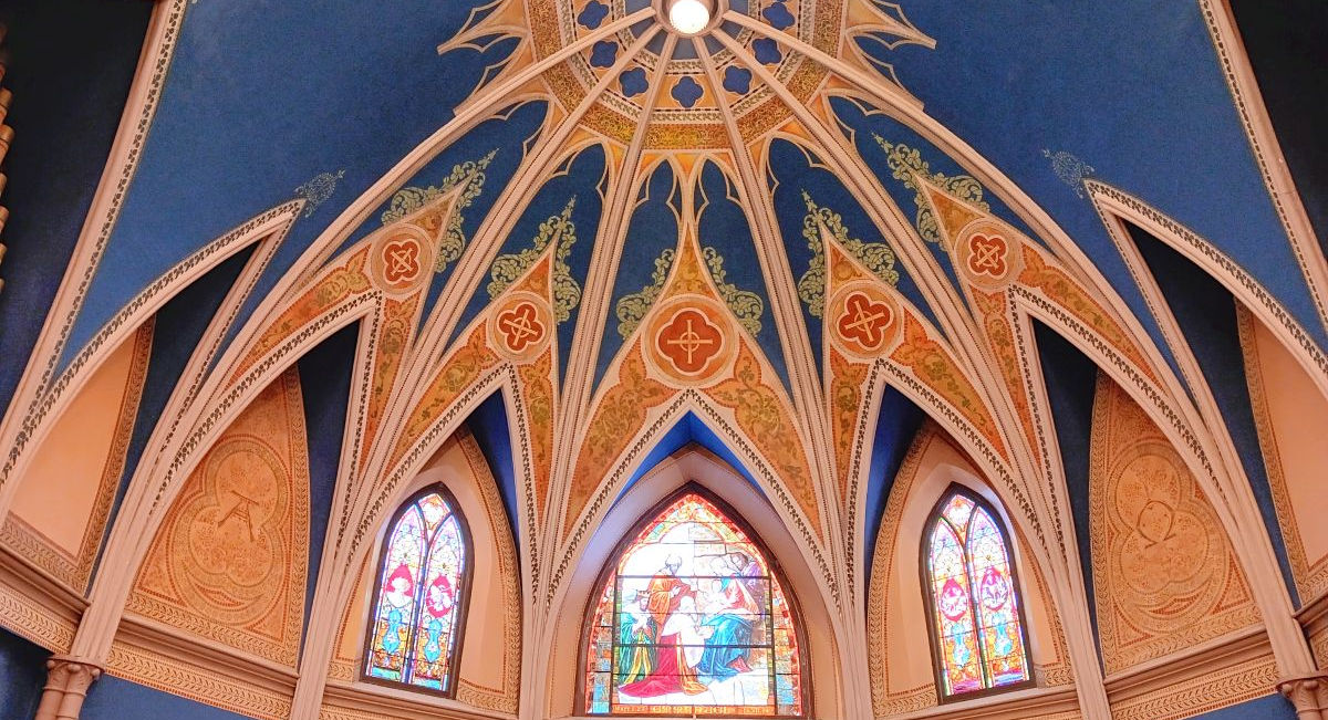 The Ornate navy vaulted ceiling of Emmanuel with gold patterns and stained glass windows