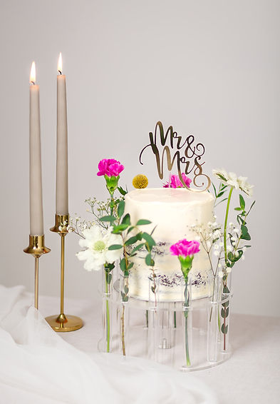 A close up photogrpah of a wedding cake created by Bake My Cake based in the Scottish Borders. The semi naked tiered wedding cake with a gold cursive Mr & Mrs cake topper.