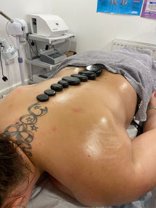 A woman lying on her stomach during a massage session with black hot stones strategically placed along her spine