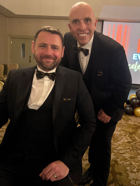 Two men smiling in suits, formal event, with bow ties, celebrating success together.