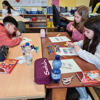 Drei Kinder sitzen an einem Gruppentisch und malen.