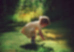 Photograph of a toddler bending over to look at something in the grass