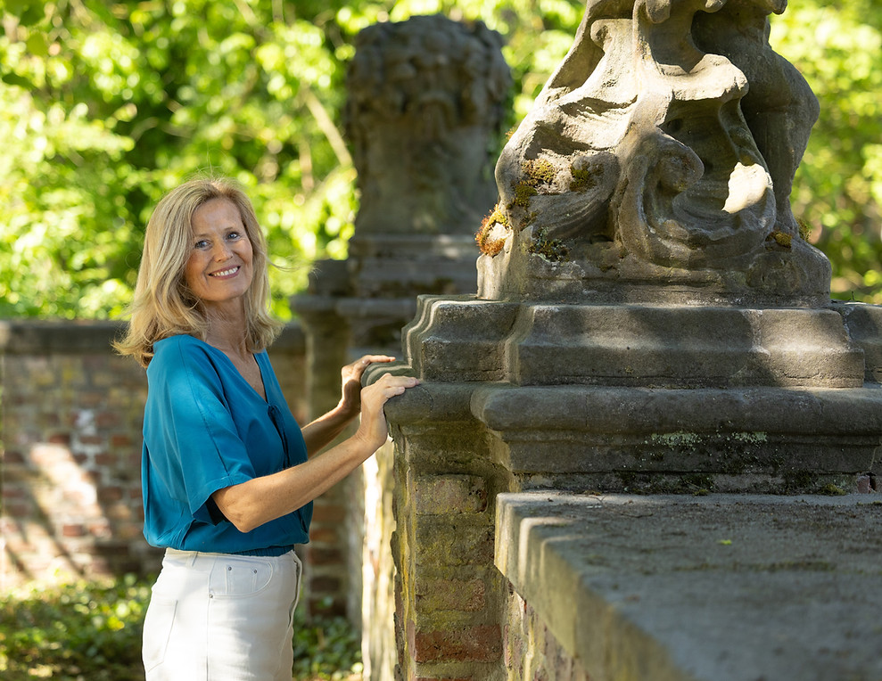 Frau in blauer Bluse lehnt entspannt an barocker Mauer.