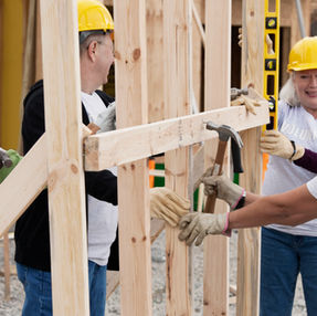    Group of four construction workers in hardhats building the framing of a home. 