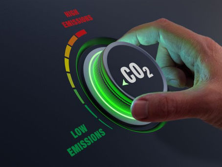 Hand turning a glowing CO2 dial from high to low emissions, symbolizing the difficulty of reducing emissions across sectors with different cost and technology barriers.