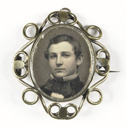 Close-up of a 19th-century brass brooch featuring a black-and-white daguerreotype portrait of a young man.