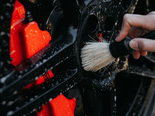 Close-up of a person cleaning a black alloy wheel with a detailing brush, illustrating car detailing vs grooming for The Detailing Specialists.