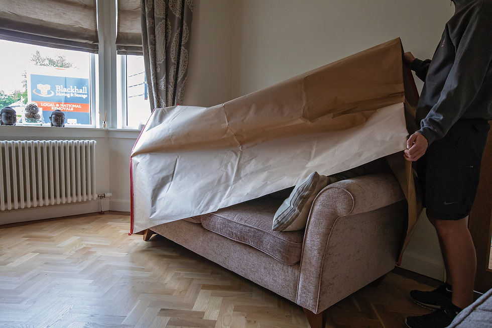 An L-shaped hex key is used to assemble a quilted grey bed frame near a door with a measuring tape on the floor.