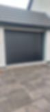 Dark grey rolling garage door on a modern building with light speckled walls and a tiled roof