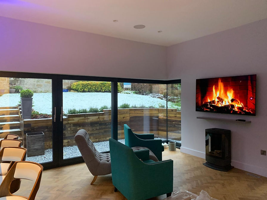 Modern living space with bi-fold doors and a wall-mounted TV displaying a fireplace scene