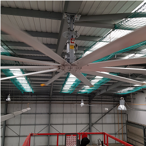 Close up view of a multi blade industrial ceiling fan mounted to warehouse roof girders