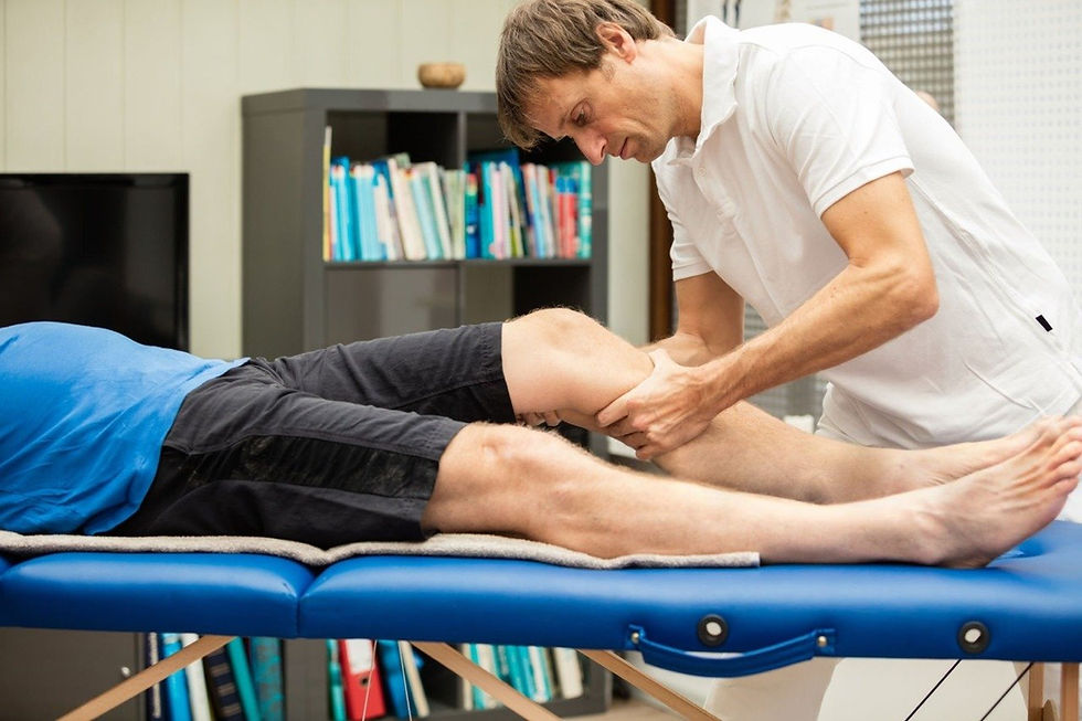 Physiotherapist in white shirt examines a patient's knee on a blue table. Bookshelf and TV in background. Setting is clinical and calm.